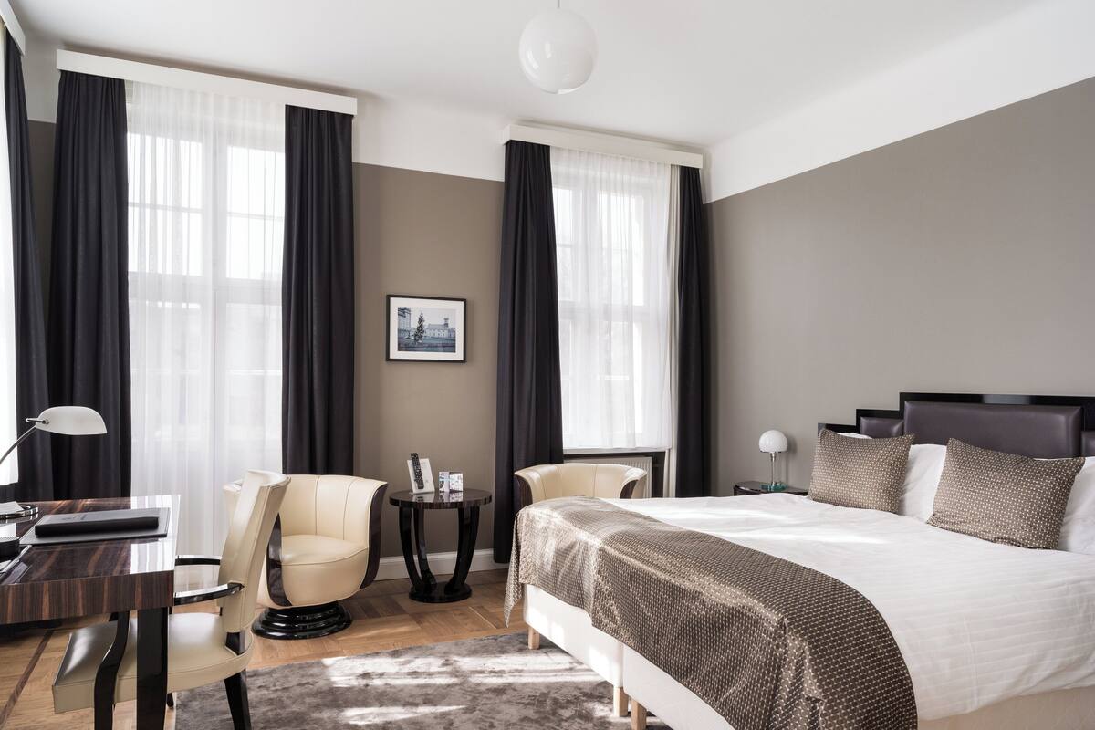 Moderni hotellihuone, jossa on suuri sänky, kaksi tuolia, pieni pöytä ja työpöytä.