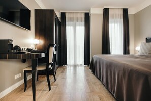 A hotel room with a bed, a desk with a chair, a TV, and a large window with curtains.