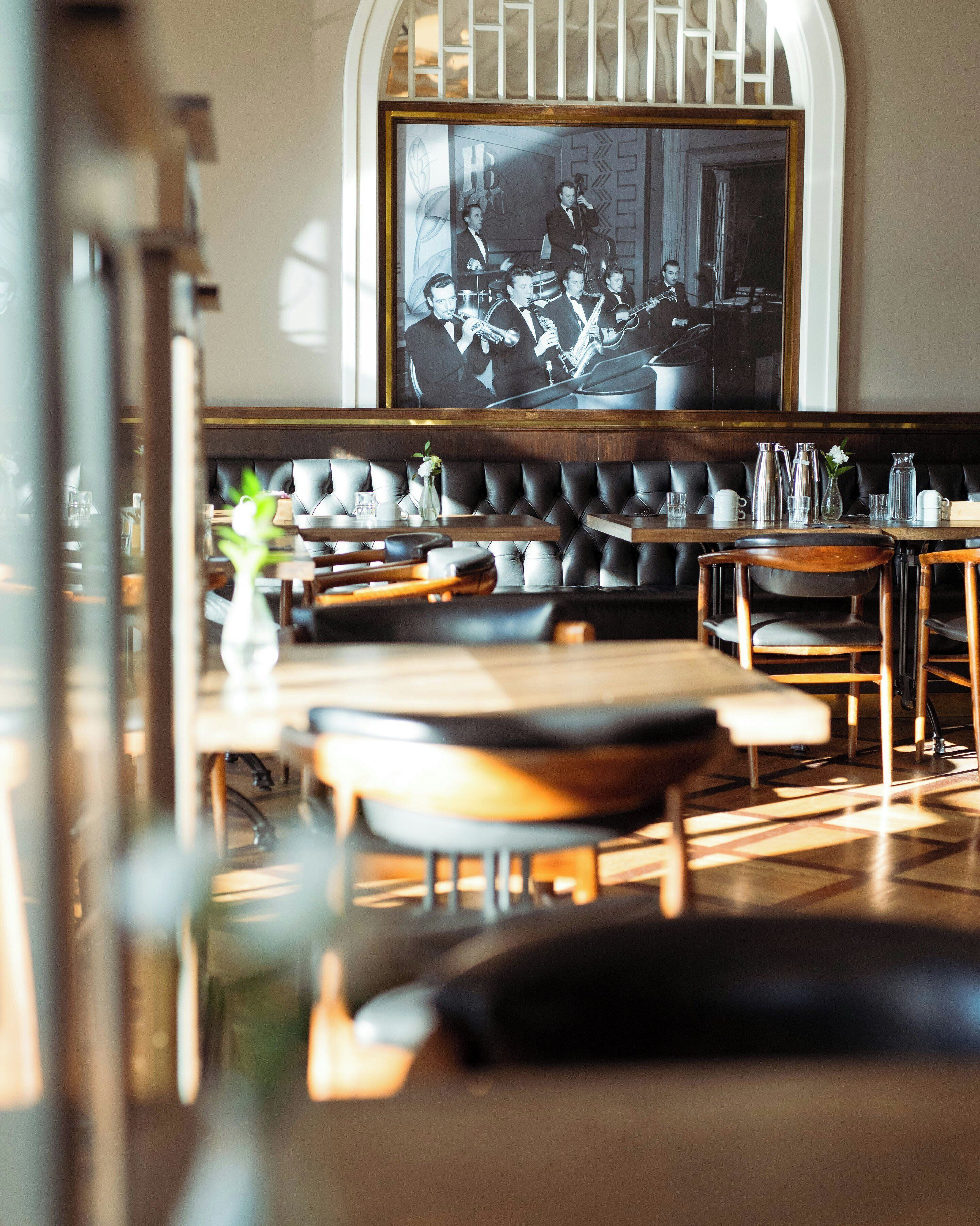 A restaurant interior with a long dining table, cushioned seating, and a large framed photograph on the wall.