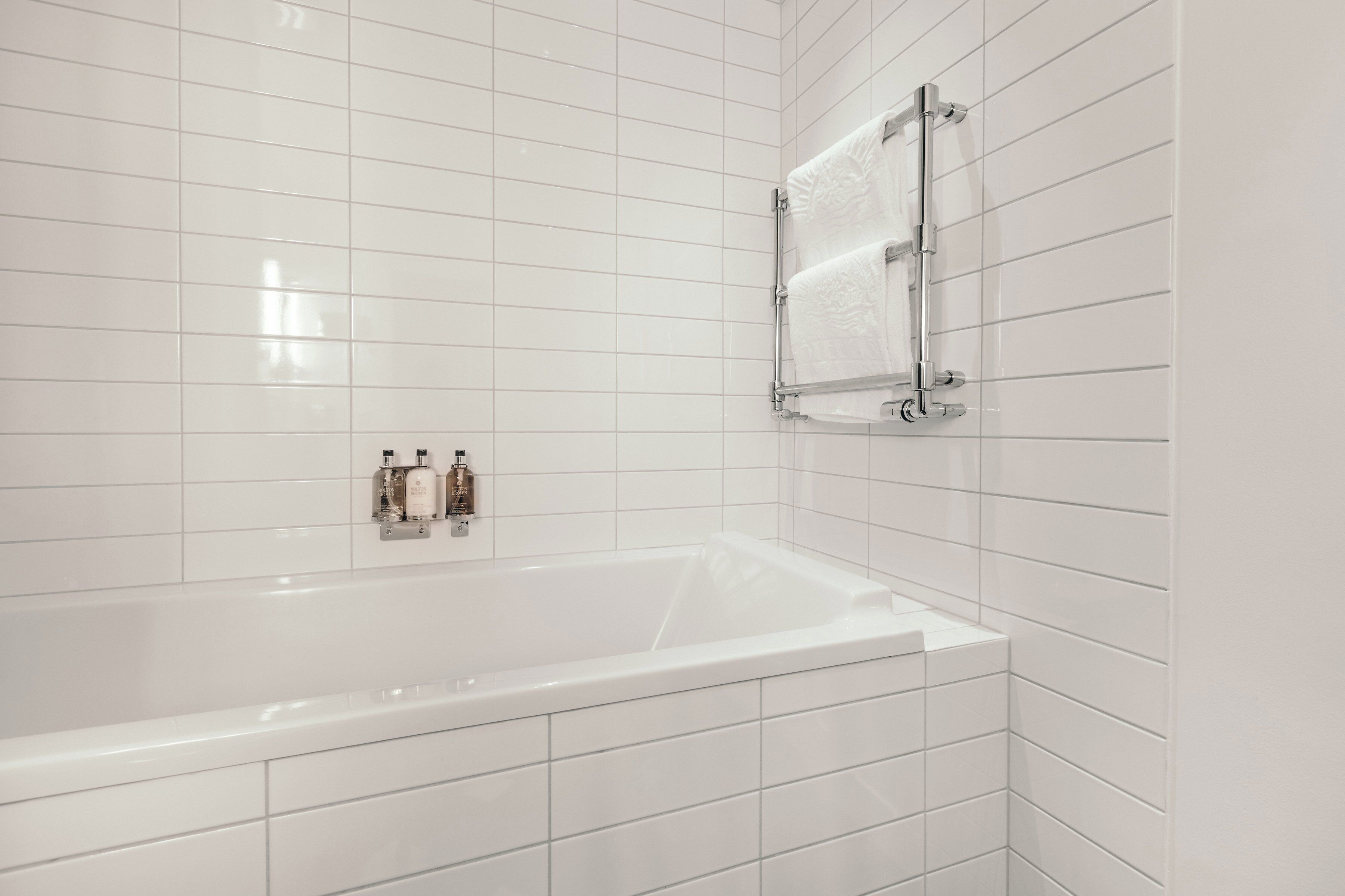 Un baño moderno con azulejos blancos, una bañera y un perchero.