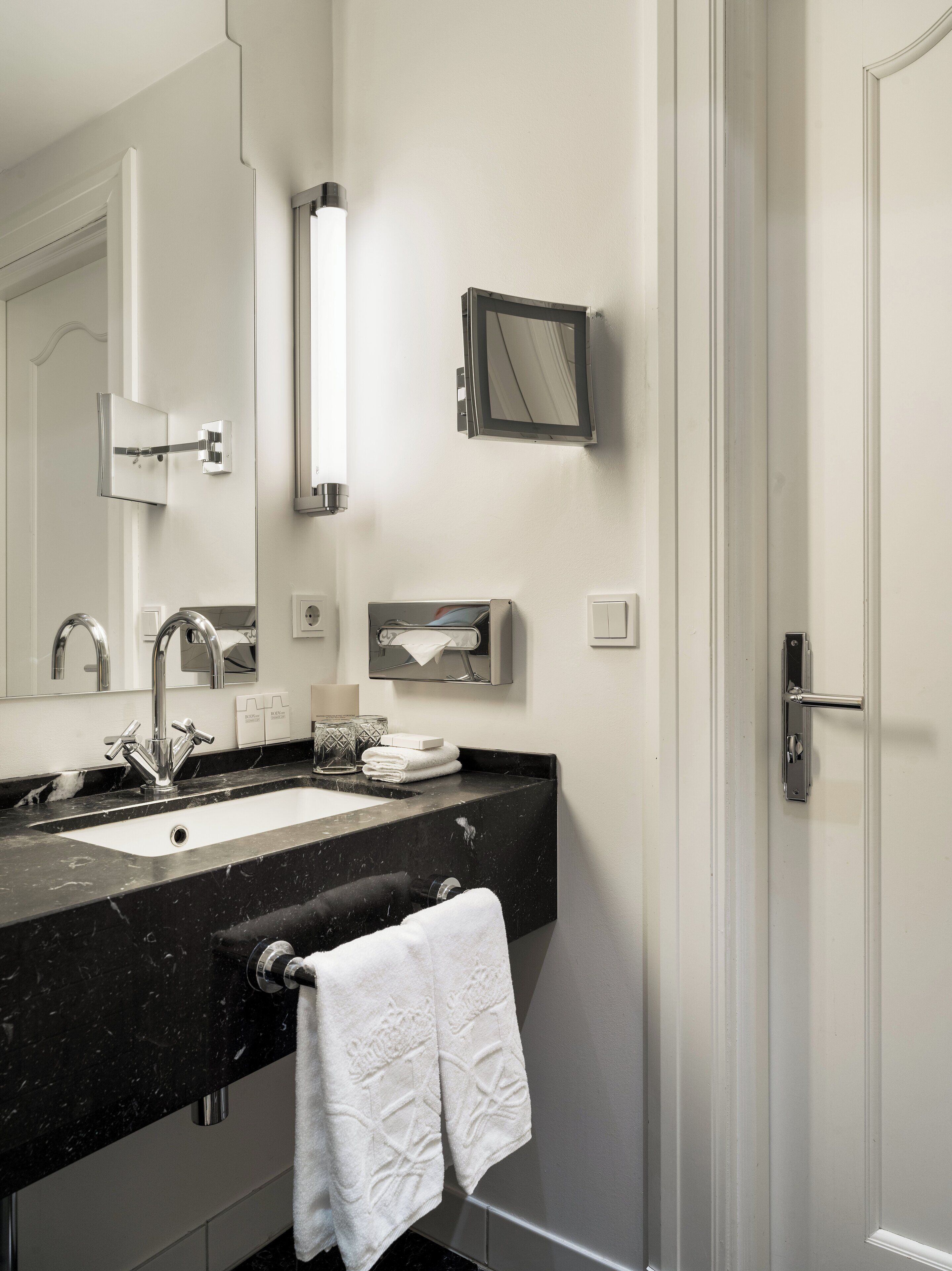 A modern bathroom with a black marble sink, a large mirror, and a towel rack.