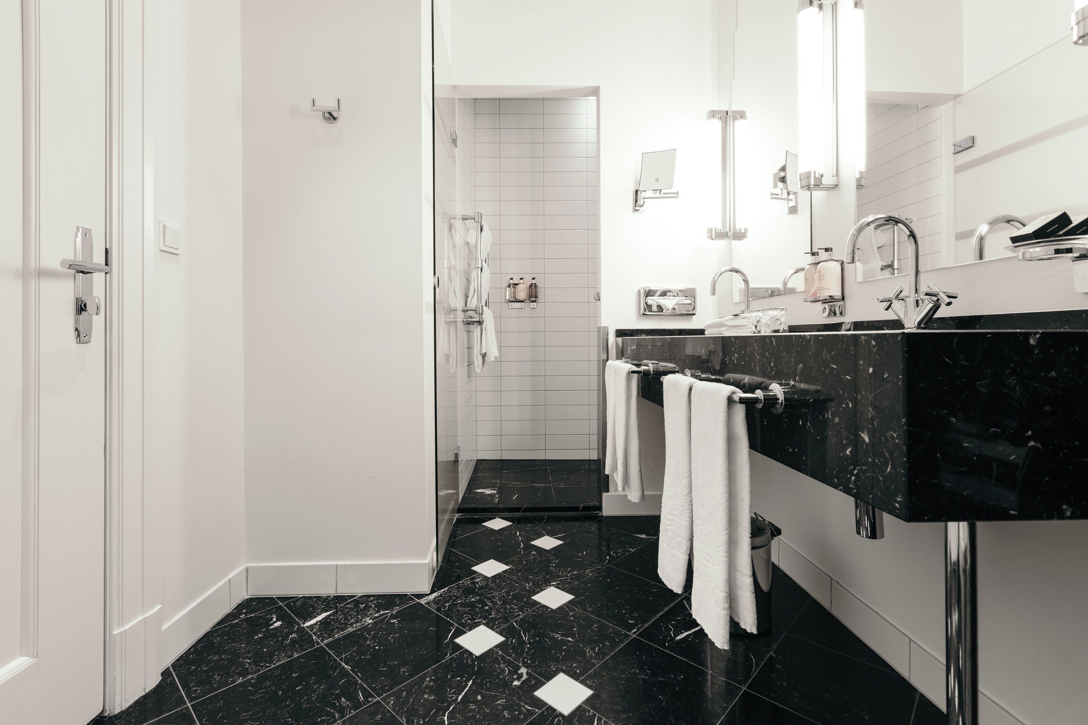Un baño moderno con suelo de mármol negro, paredes blancas y encimera negra.