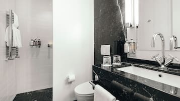 A modern bathroom with a black marble countertop, a white toilet, and a glass shower enclosure.