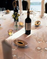 A table set for dining with a bottle of wine, candles, and a vase with flowers.