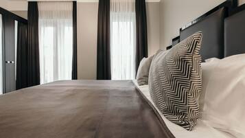 A modern hotel room with a large bed, dark curtains, and a chevron-patterned pillow.
