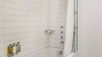 A modern bathroom with white tiled walls, a glass shower enclosure, a bathtub, and three hand soap dispensers mounted on the wall.