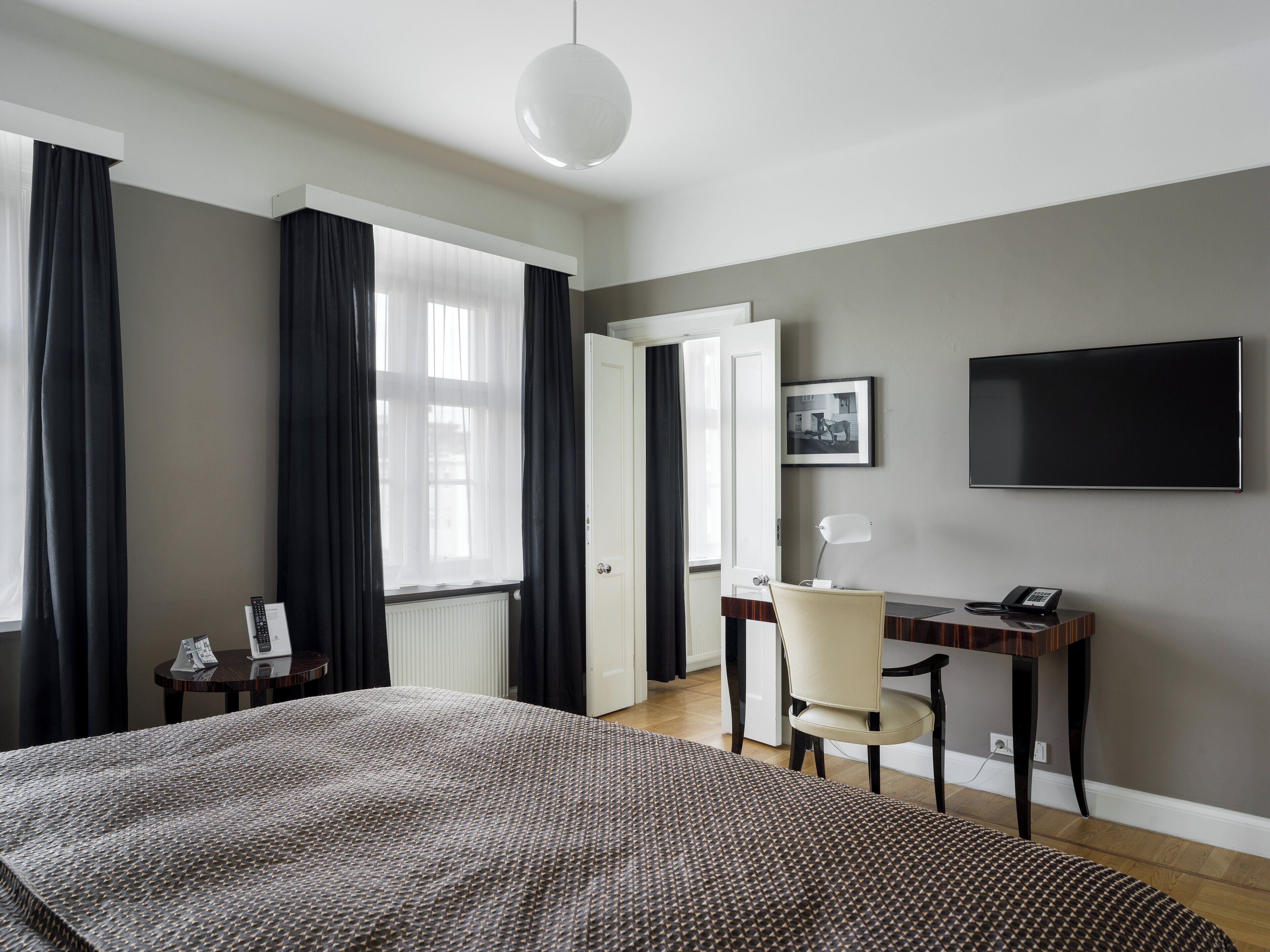 A hotel room with a bed, a desk, a chair, a TV, and a window with curtains.