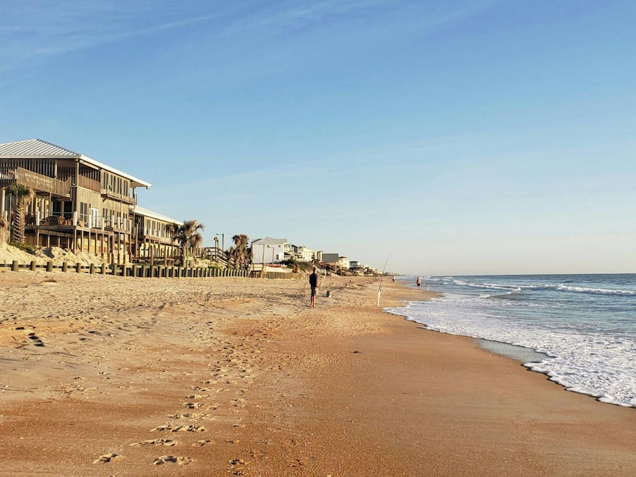 Una playa con un edificio de madera, una orilla arenosa y cielo despejado.