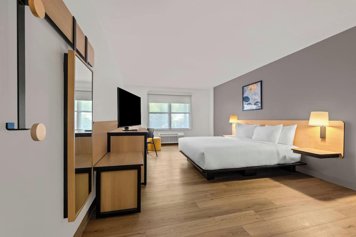 A modern hotel room with a bed, bedside lamps, a TV, a desk, and a large mirror.