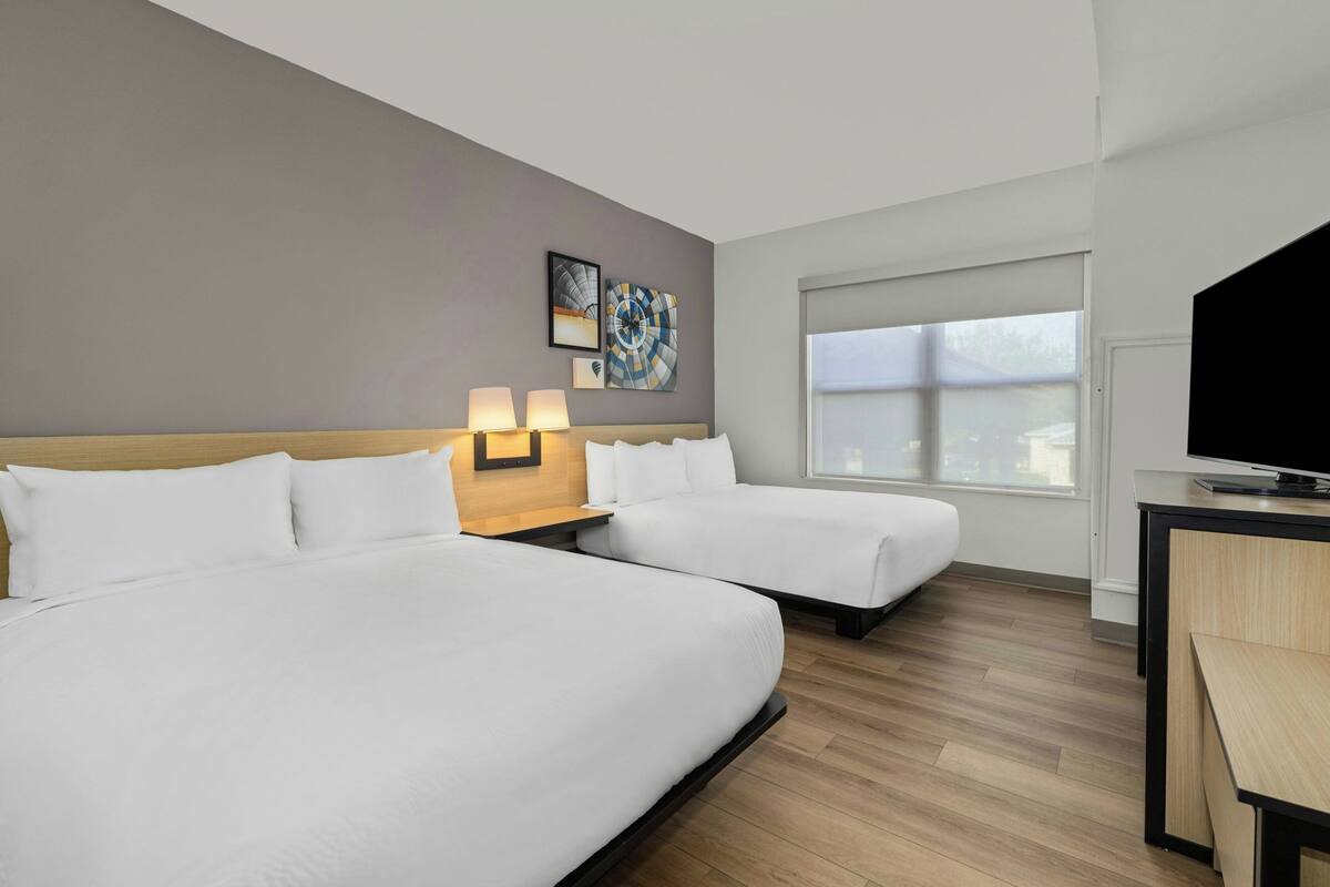 A hotel room with two beds, a desk, a TV, and a window.