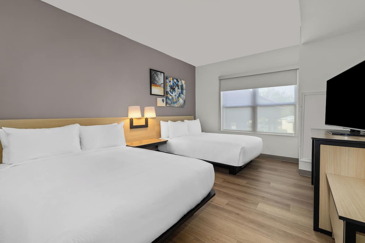 A hotel room with two beds, a desk, a TV, and a window.