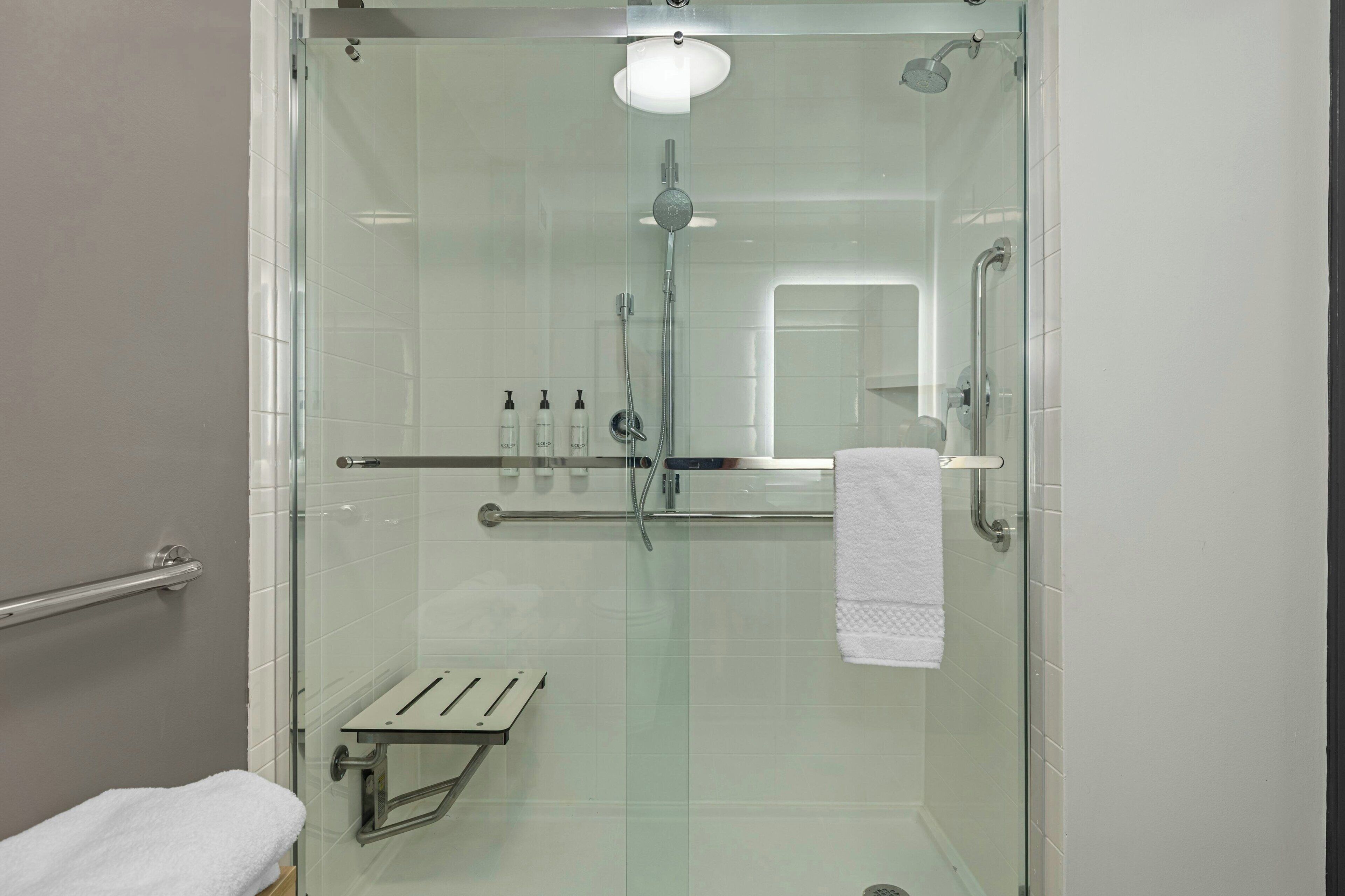 Eine Duschkabine mit Glaswänden, einer Handbrause, einer Glastür, einem weißen Handtuch und einem Glasregal mit Toilettenartikeln.