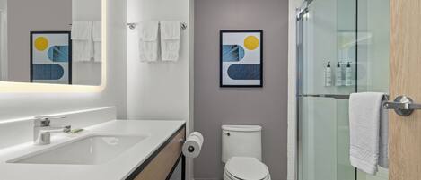 Un baño moderno con cabina de ducha de vidrio, un lavabo blanco y un inodoro.
