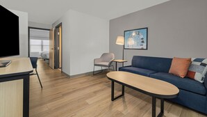 Una habitación de hotel moderna con suelo de madera, un sofá, una mesita, una silla y un televisor.