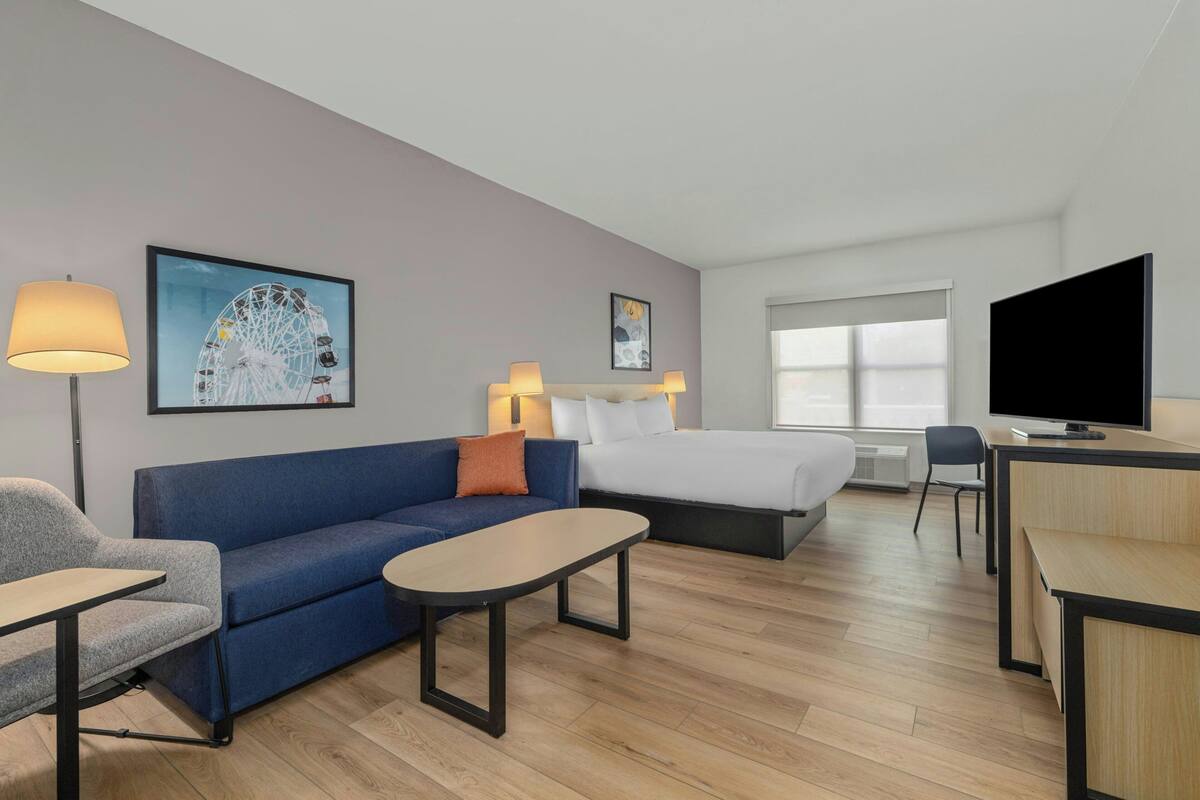 A hotel room with a bed, a sofa, a desk, a TV, and artwork on the walls.