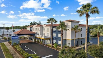 A hotel with a parking lot, a covered entrance, and palm trees.