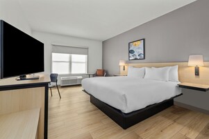 A modern hotel room with a large bed, a flat-screen TV, a desk, and a chair.