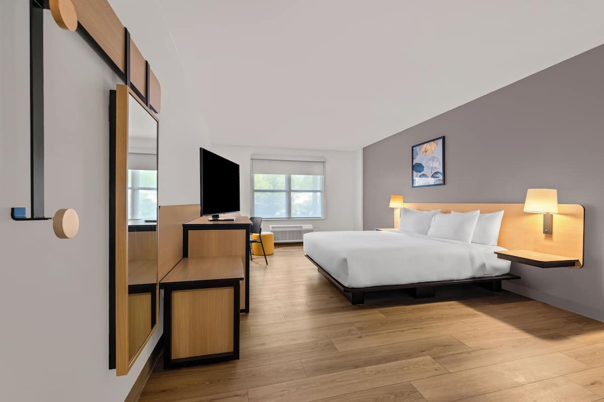 A modern hotel room with a bed, bedside table, TV, and a large mirror.