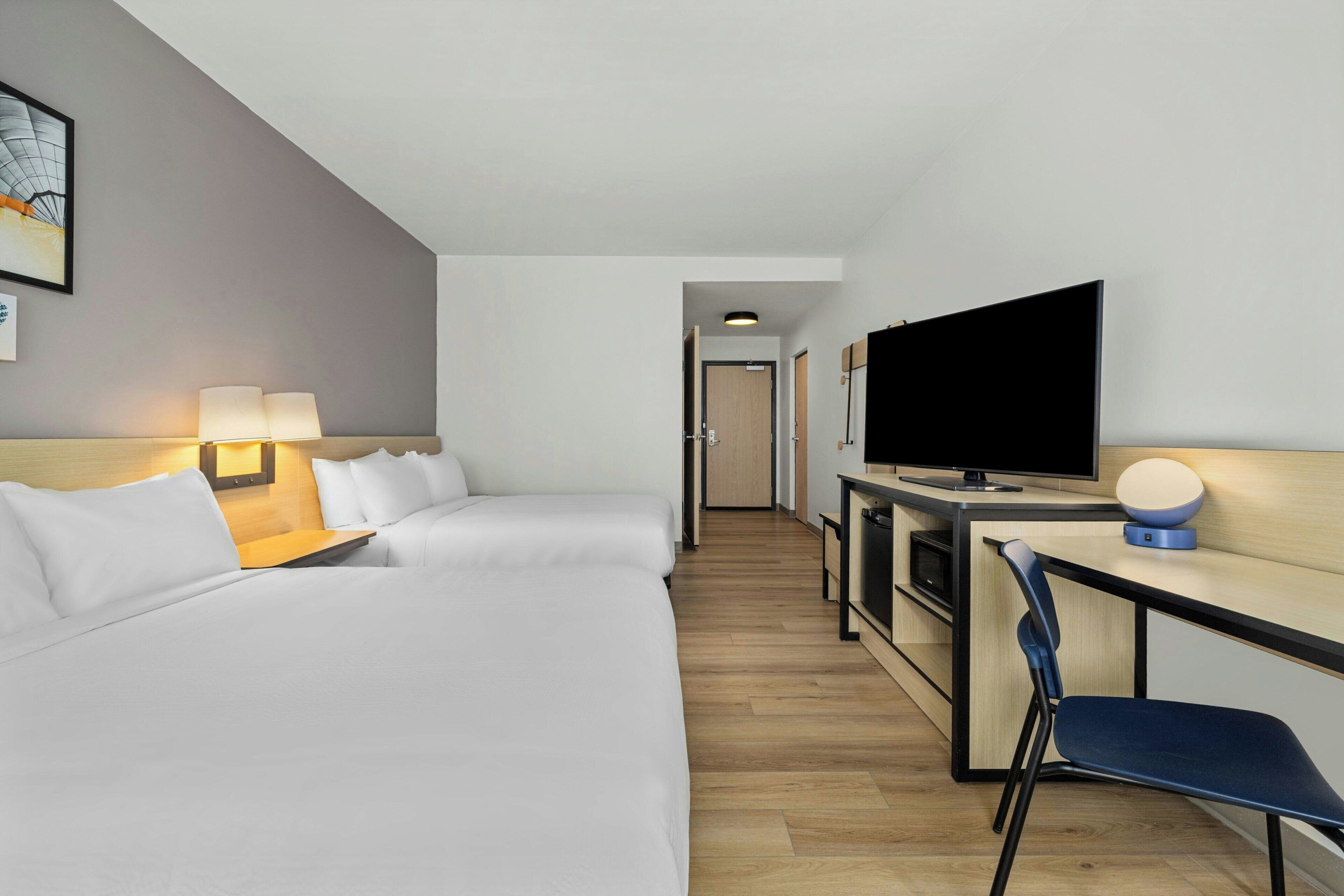 Et hotelværelse med en seng, et skrivebord med fjernsyn, en stol og en lampe.