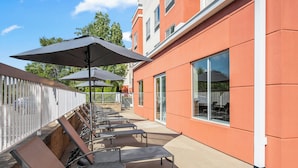 A covered outdoor seating area with lounge chairs and umbrellas, adjacent to a building with large windows. - Fairfield Inn and Suites by Marriott Marion (Marion)
