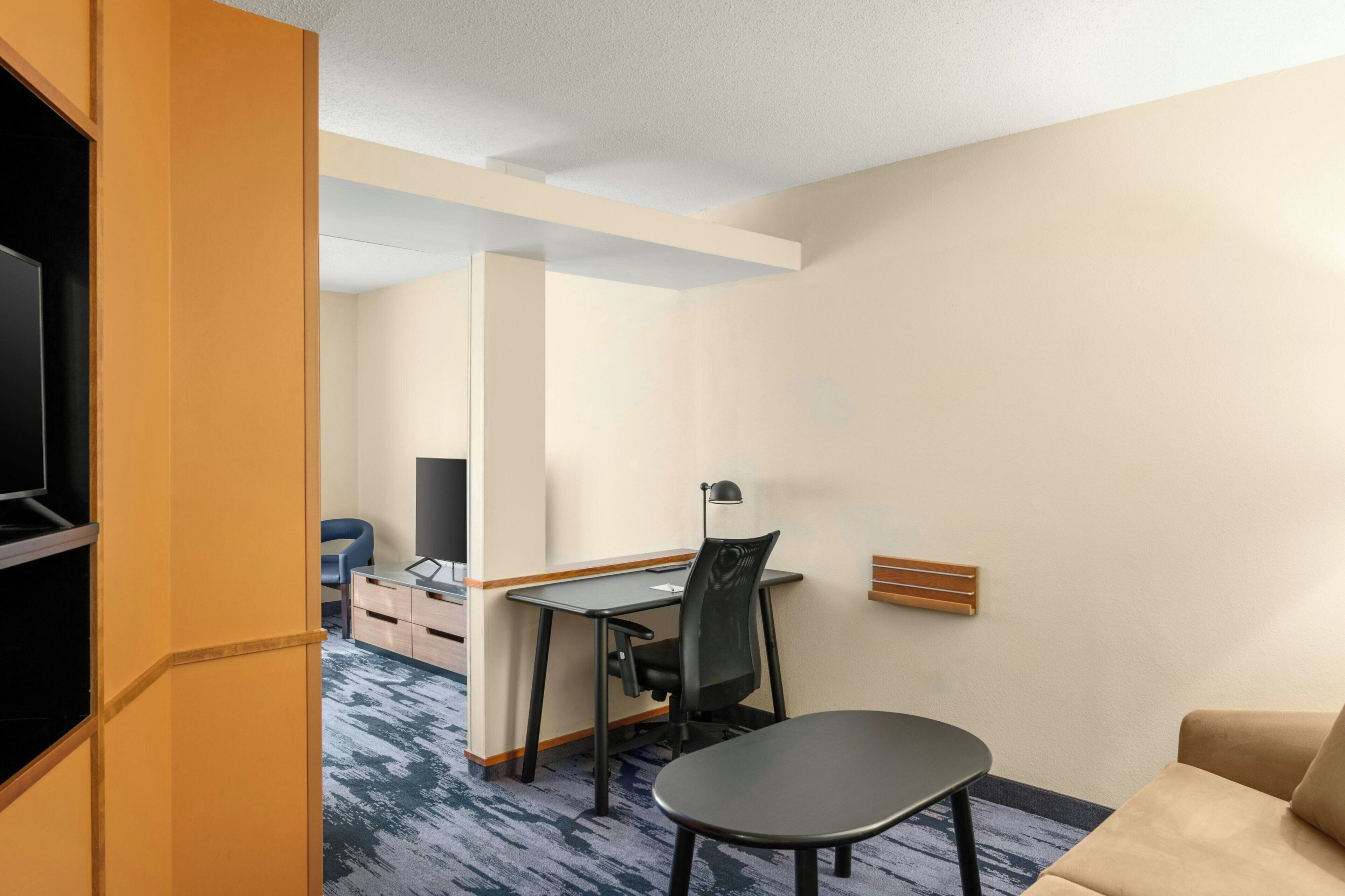 A hotel room with a desk, chair, and a sofa.