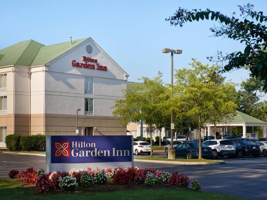 Een Hilton Garden Inn hotel met een bord, parkeerplaats en omliggend groen.