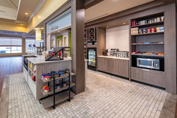 Un moderno vestíbulo de hotel con una zona de cafetería, una sección refrigerada y una kitchenette con microondas.