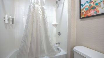Une salle de bain avec une baignoire, une douche et des toilettes. Trois flacons de produits de toilette sont posés sur le mur.