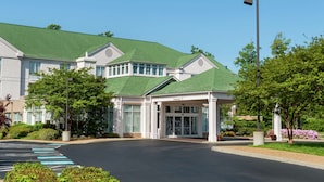 A building with a green roof, a covered entrance, and a parking lot with marked spaces. - Hilton Garden Inn Newport News (Newport News)