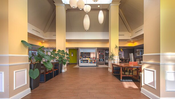 A spacious lobby with a central reception area, large potted plants, and a wooden floor. - Hilton Garden Inn Newport News (Newport News)