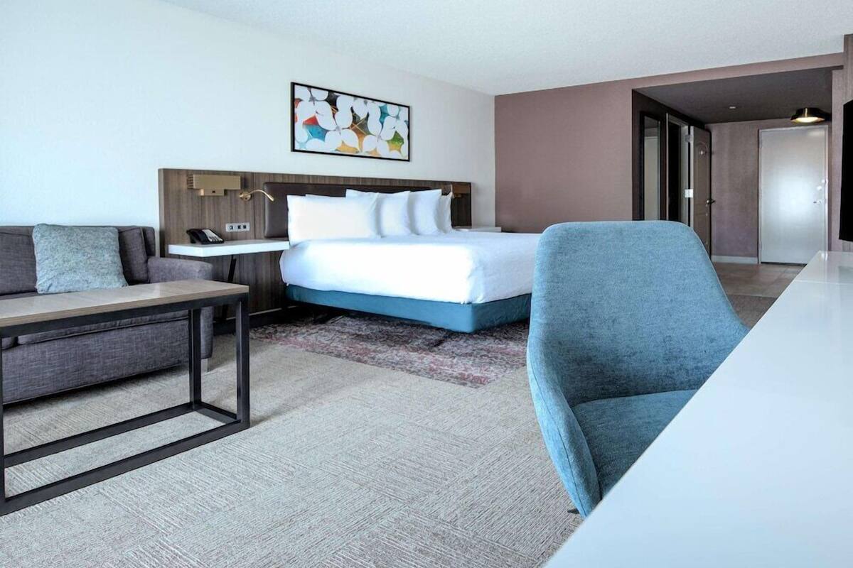 Una habitación de hotel con cama, escritorio, silla, sofá y un cuadro en la pared.