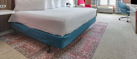 Quarto de hotel com uma cama grande, uma escrivaninha, uma cadeira, uma luminária de mesa, um telefone e uma janela com cortinas.