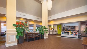 A spacious lobby with a central seating area, a refreshment counter, and large potted plants. - Hilton Garden Inn Newport News (Newport News)