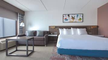 Una habitación de hotel moderna con una cama grande, un sofá, una mesita y un televisor montado en la pared.