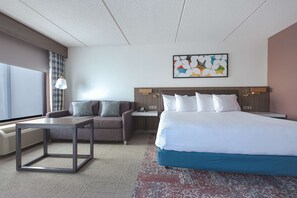 Une chambre d’hôtel moderne avec un grand lit, un canapé, une petite table et un téléviseur fixé au mur.