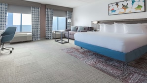 A hotel room with a large bed, a desk, a chair, and a window with curtains. - Hilton Garden Inn Newport News (Newport News)
