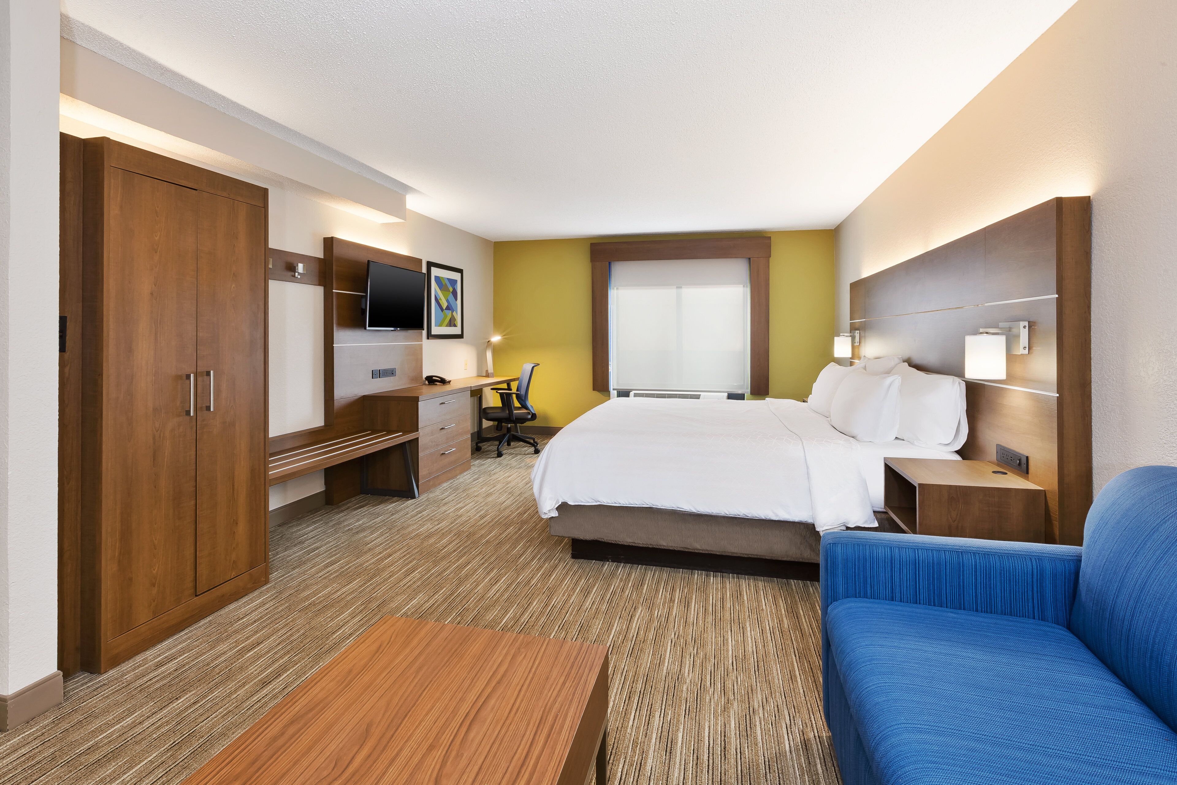 A hotel room with a bed, a desk with a chair, a television, and a sofa.