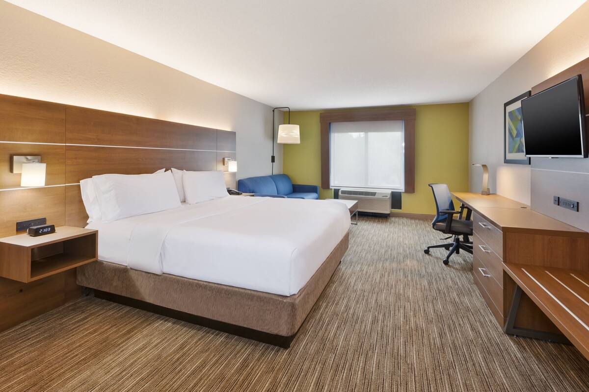 A hotel room with a large bed, a desk, a chair, a flat-screen TV, and a window.