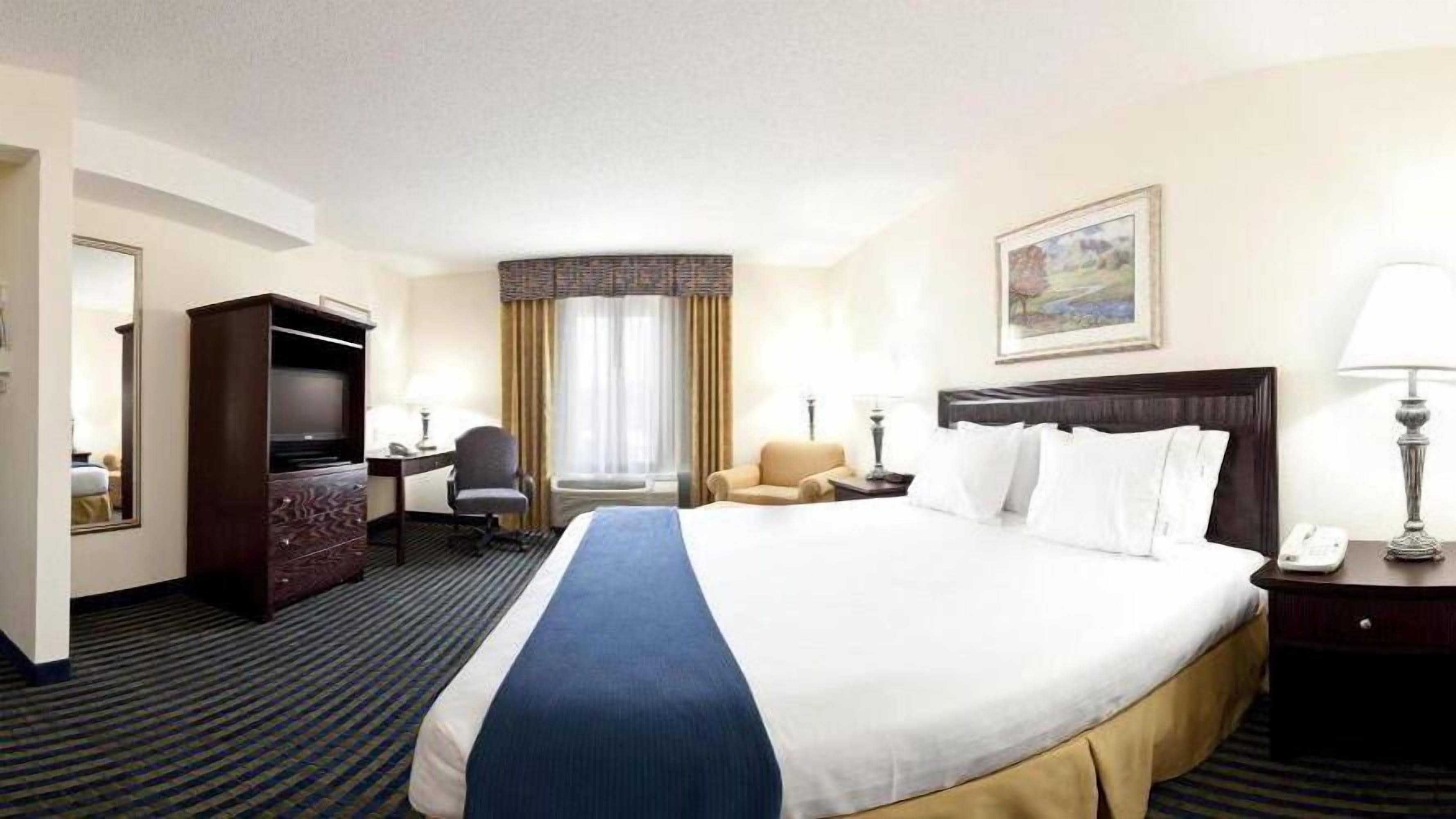 Une chambre d’hôtel avec un grand lit, un bureau avec une chaise, une télévision et un tableau au mur.