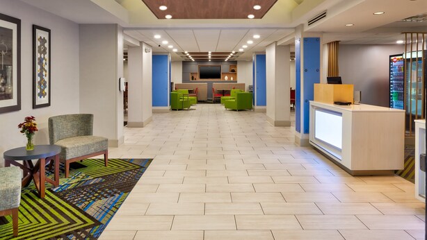 A spacious lobby with a reception desk, green seating, and a large TV screen. - Holiday Inn Express Hotel & Suites Chesapeake by IHG (Chesapeake)