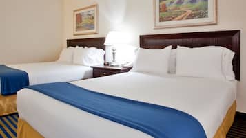 Ein Hotelzimmer mit zwei Betten, jeweils mit weißer Bettwäsche und blauen Akzenten. An den Wänden hängen zwei Gemälde, ein Nachttisch mit Lampe und ein Telefon.