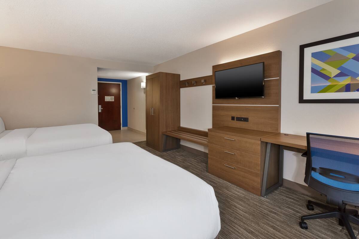 A hotel room with two beds, a desk with a computer, a TV, and a framed picture on the wall.