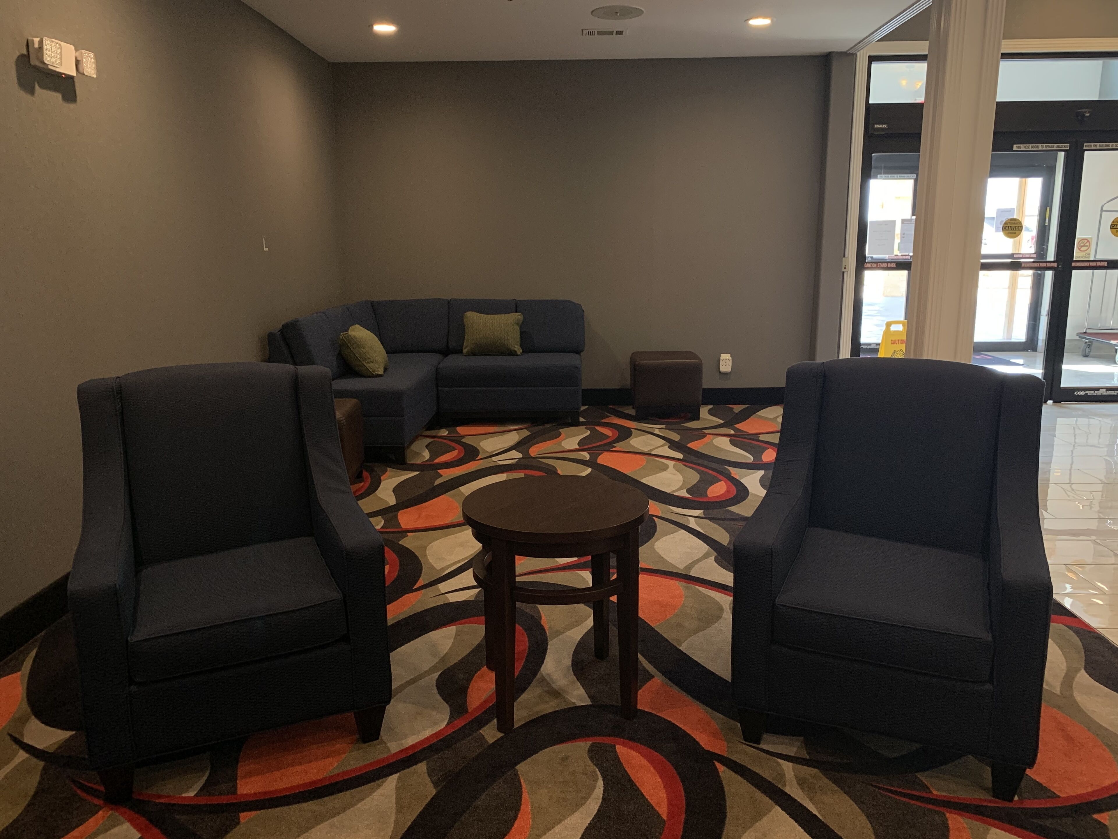 A hotel lobby with a sectional sofa, two armchairs, a small round table, and a patterned carpet.