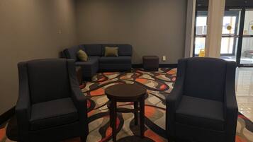 A hotel lobby with a sectional sofa, two armchairs, a small round table, and a patterned carpet.