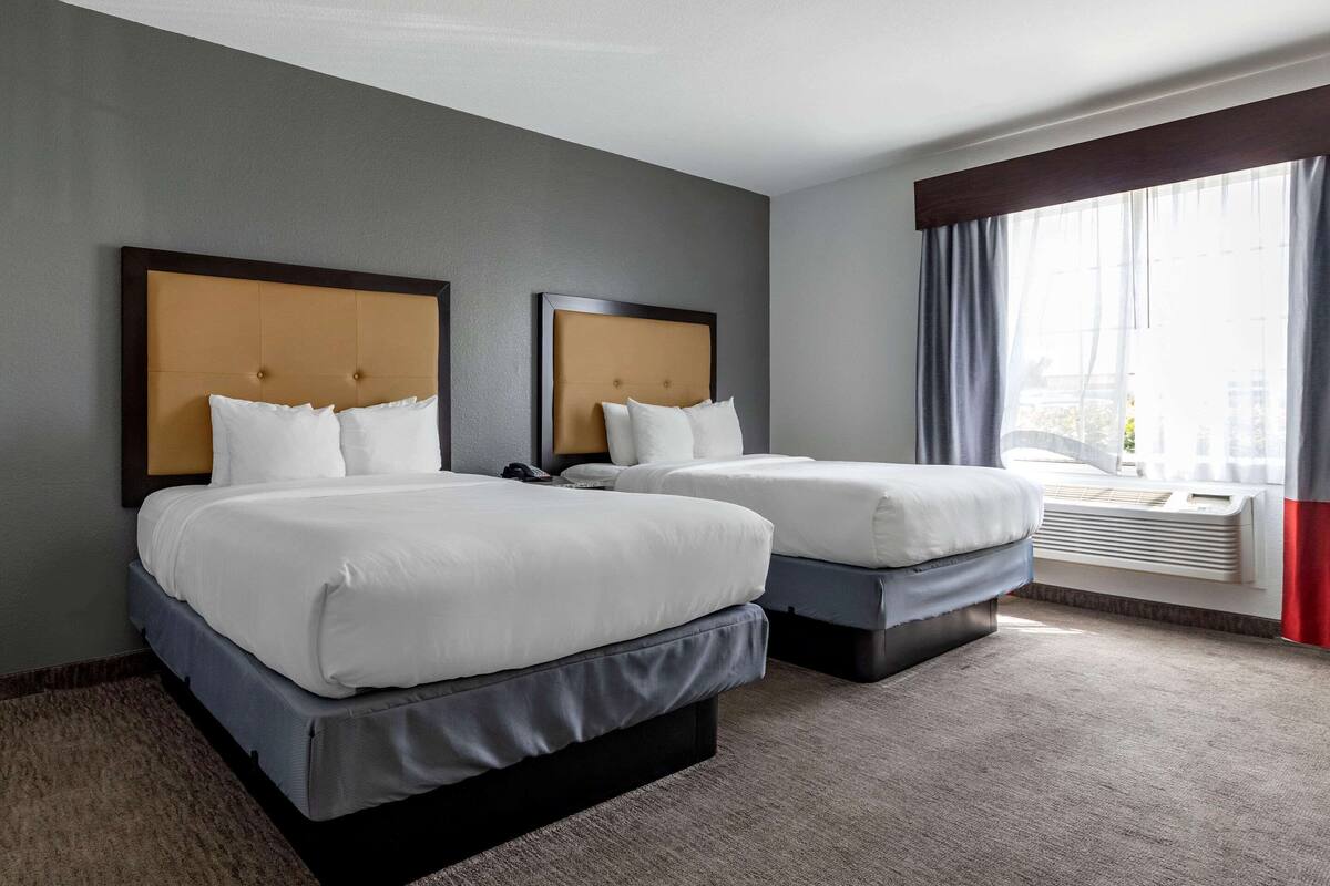 A hotel room with two beds, a large window with curtains, and a built-in air conditioning unit.