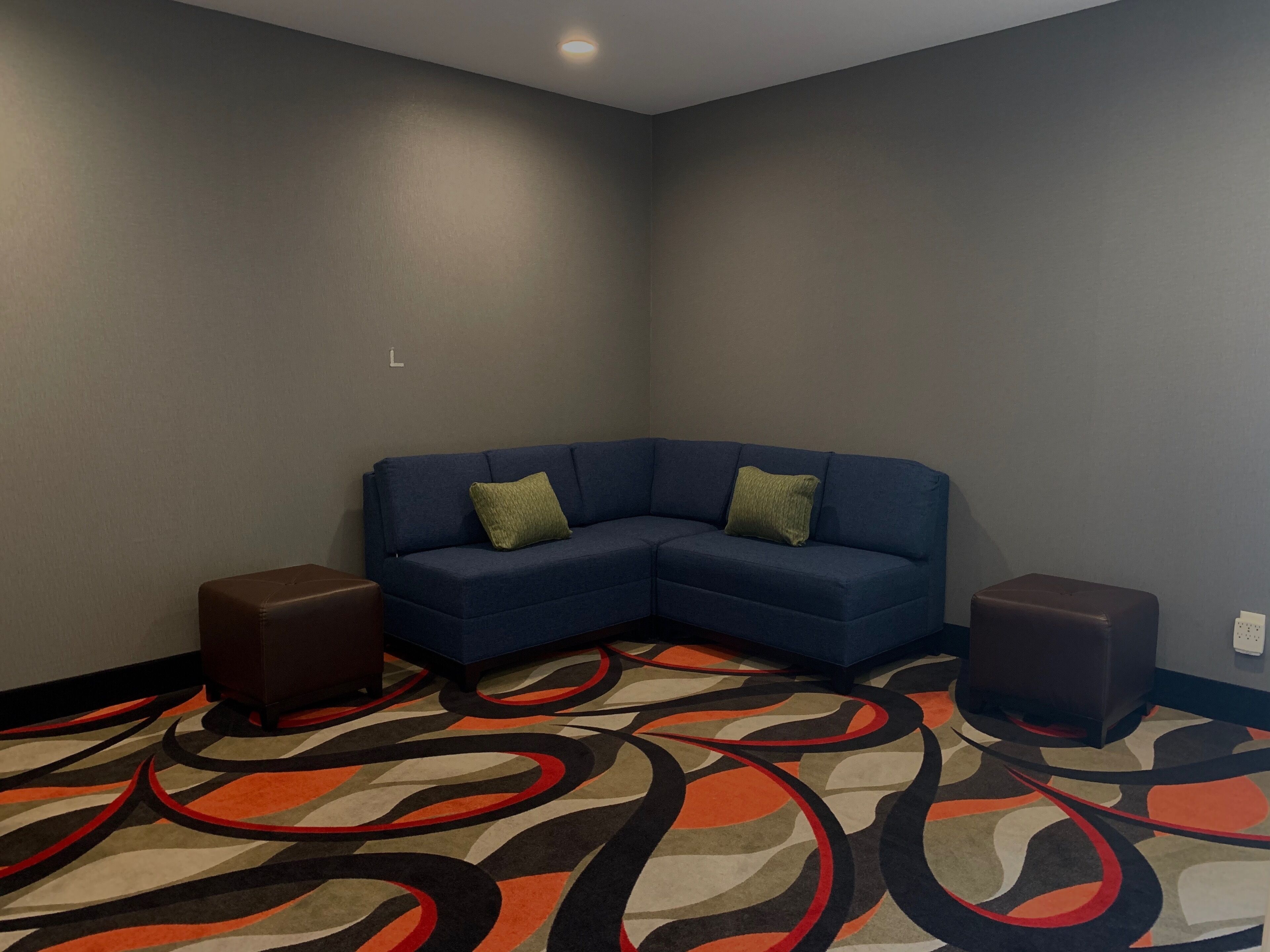 Quarto de canto com um sofá azul em forma de L, dois pufes marrons e um tapete estampado.