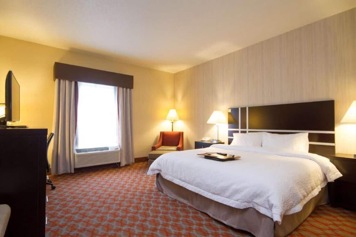 Une chambre d’hôtel avec un grand lit, un bureau, une chaise, une télévision et une fenêtre avec des rideaux.