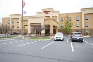 A hotel with a sign reading "Hampton Inn." There are two cars parked in the lot, and a flagpole with an American flag is visible.