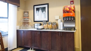 Ein Frühstücksbuffet in einem Hotel mit Kaffeemaschine, Saftspender und verschiedenen Speisenbehältern.