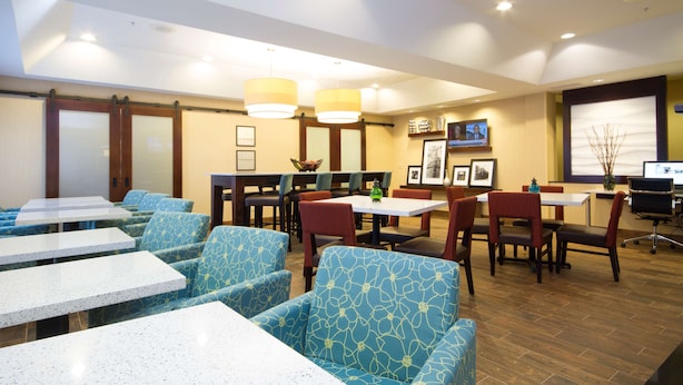 Ein Hotelrestaurant mit blauen gemusterten Stühlen, weißen Tischen und einem Fernseher an der Wand.
